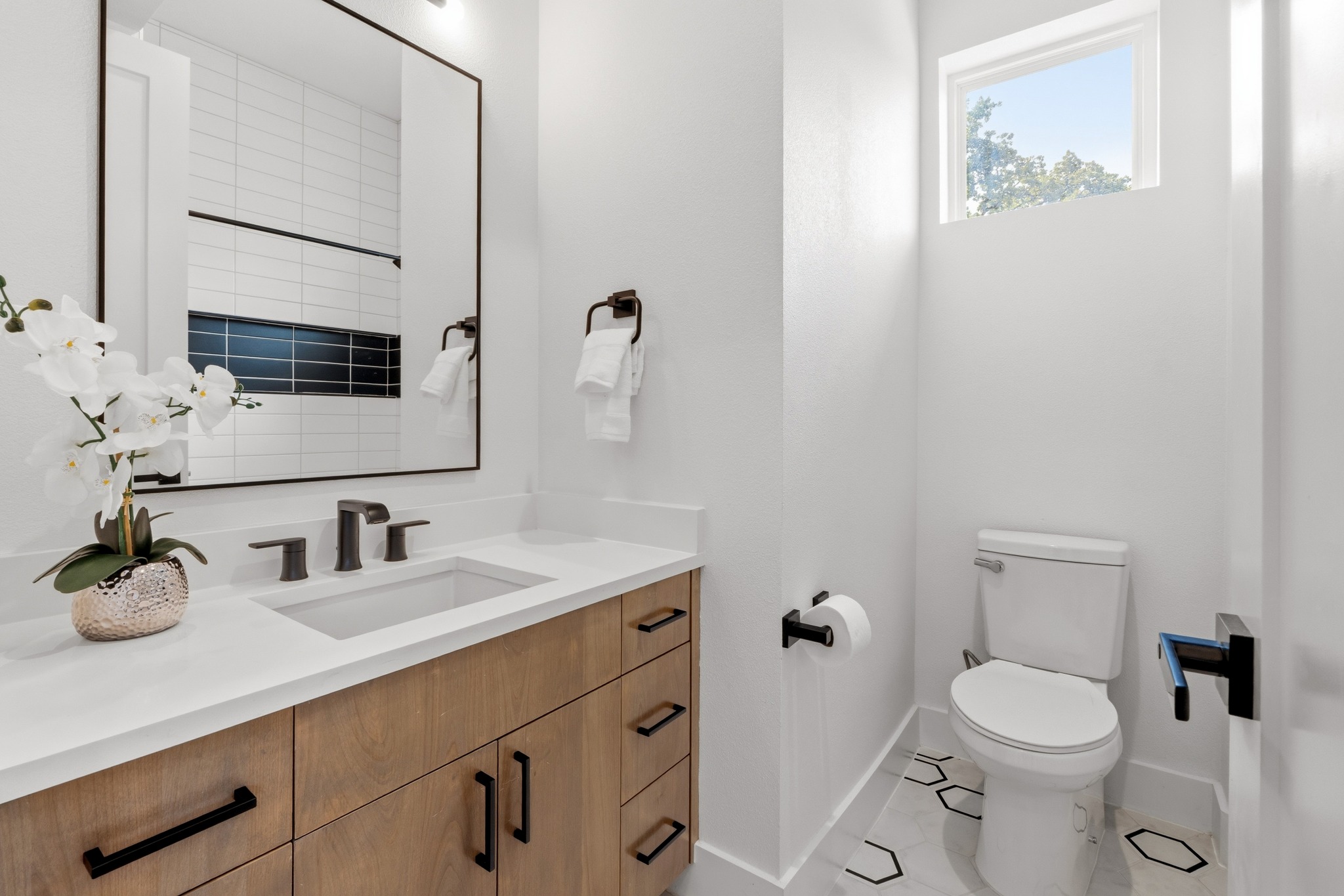 3304 East 17th Street, Unit B Austin, TX 78721 - Photo 24 of 35 Modern hall bathroom adjacent to two secondary bedrooms featuring sleek wooden cabinetry, a crisp white quartz vanity, and geometric floor tiling.