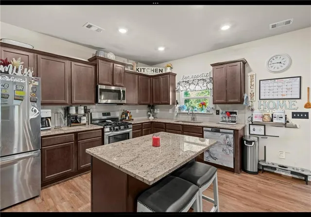 a kitchen with stainless steel appliances granite countertop a refrigerator a sink dishwasher a stove top oven a kitchen island and chairs with wooden floor