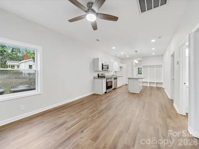 an empty room with wooden floor chandelier fan and windows
