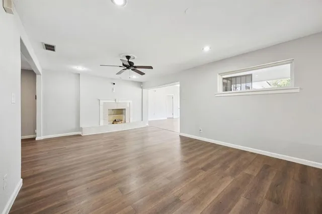 a view of an empty room with wooden floor and a ceiling fan