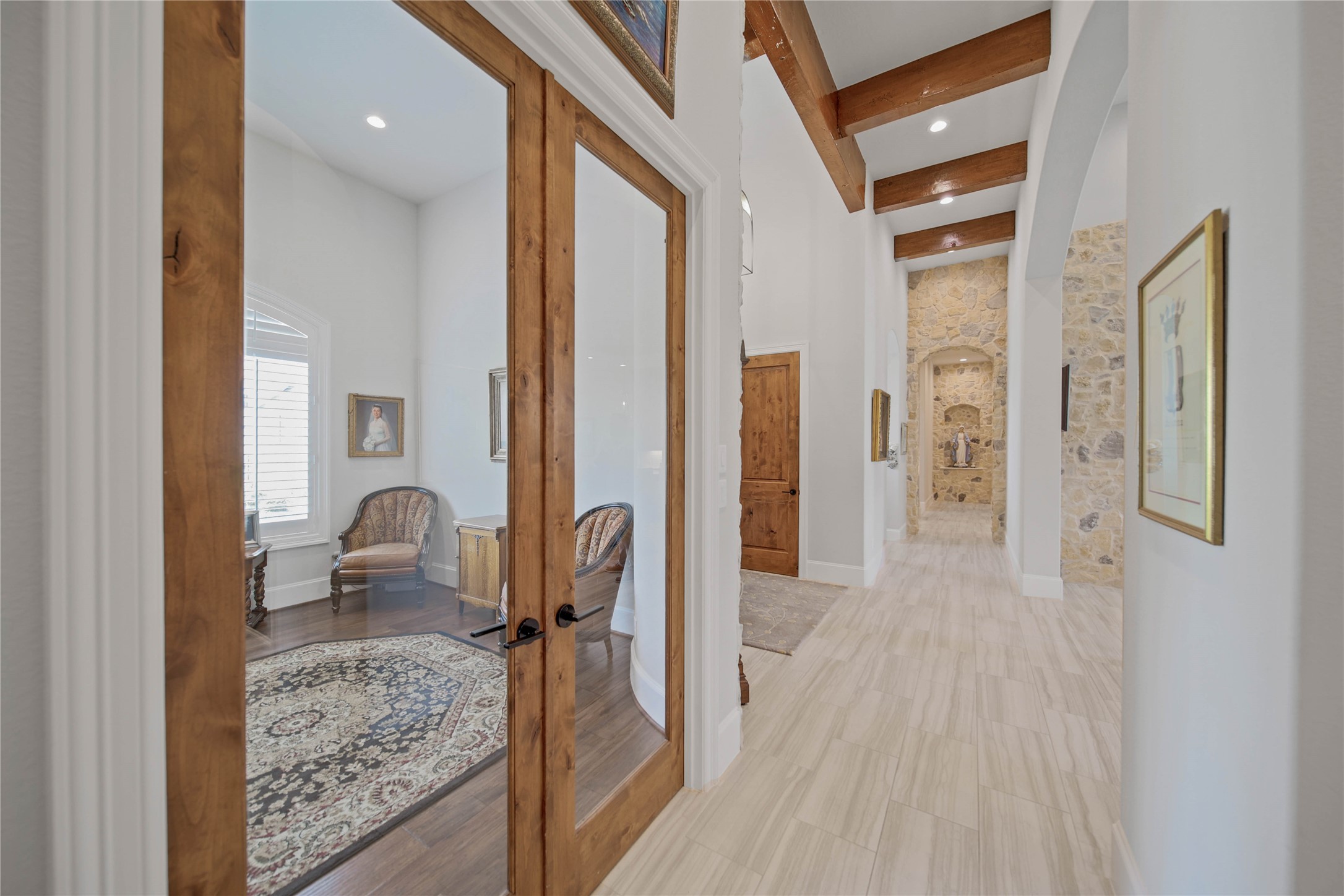 The elegant hallway features beautiful wooden beams and stone accents, leading to a cozy room with double glass doors, rich wood flooring, and abundant natural light.