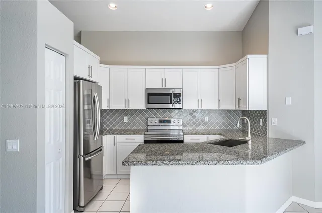 a kitchen with stainless steel appliances granite countertop a refrigerator a stove a sink and white cabinets