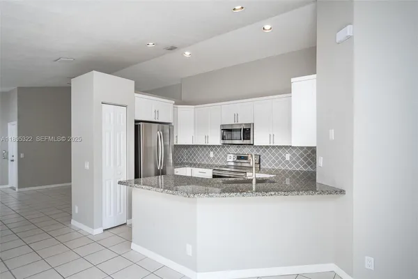 a kitchen with stainless steel appliances granite countertop a refrigerator a stove a sink and white cabinets