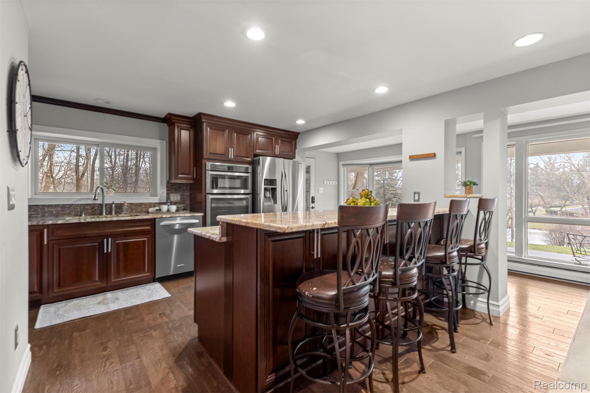 45401 West 9 Mile Road Novi, MI 48374 - Photo 16 of 67 Kitchen with light stone countertops, a kitchen bar, appliances with stainless steel finishes, dark brown cabinetry, and dark wood-style floors