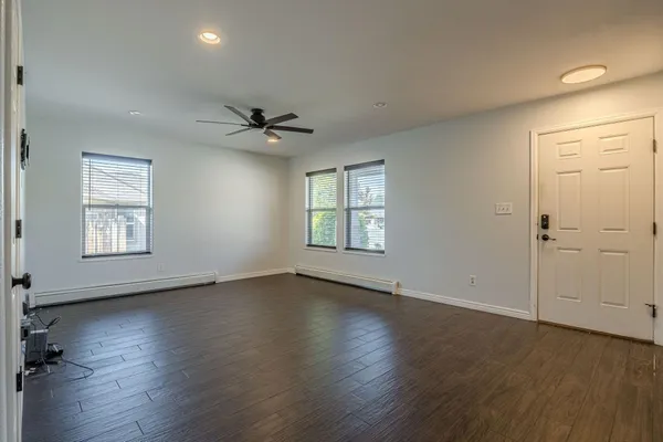 an empty room with wooden floor chandelier fan and windows
