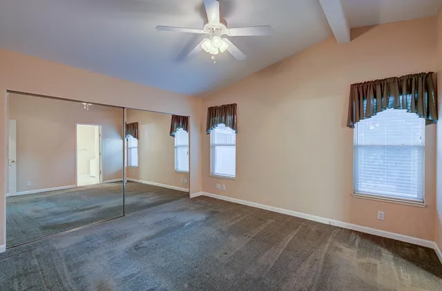 an empty room with a chandelier fan and windows