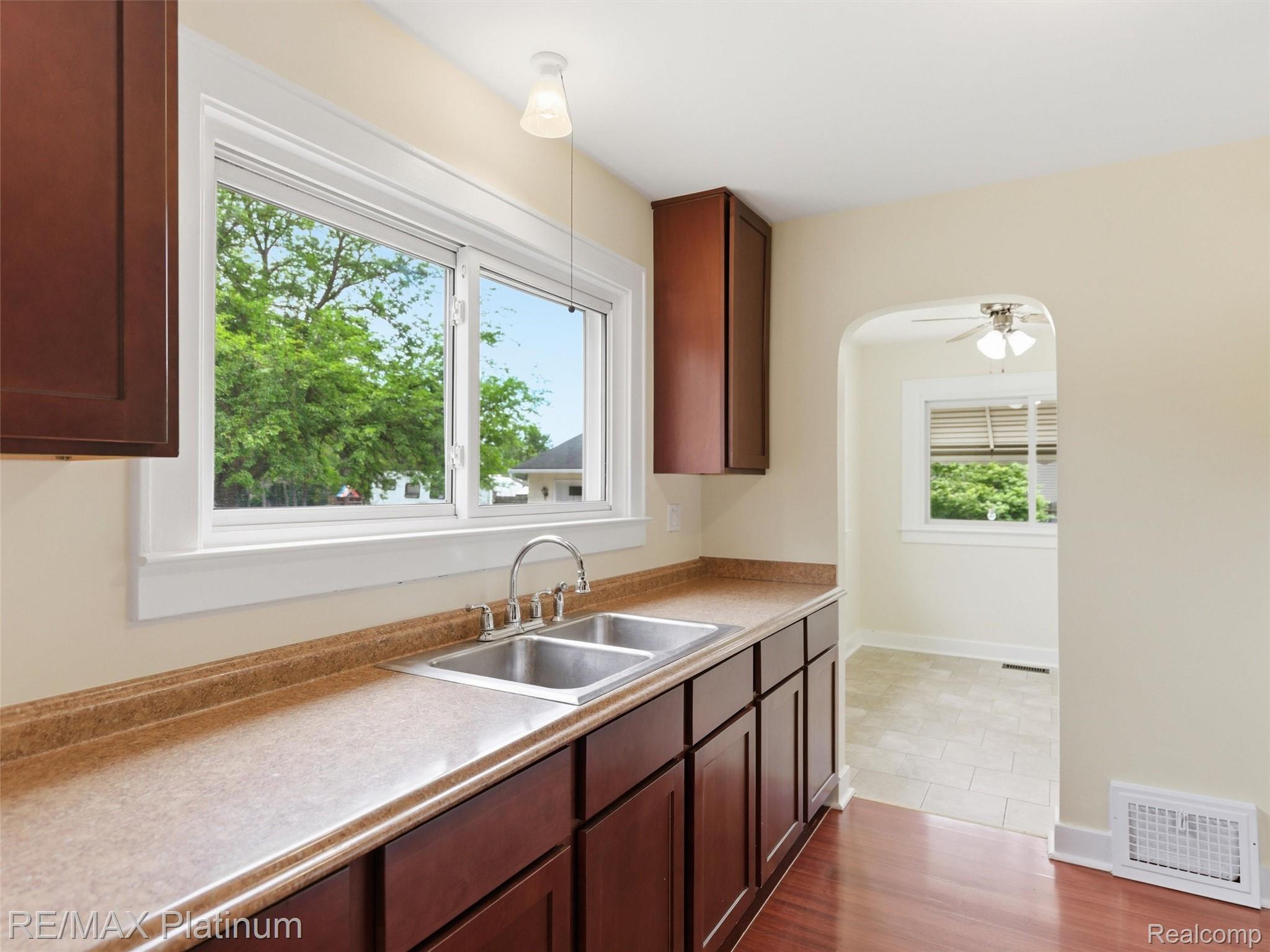 6335 Silver Lake Road Linden, MI 48451 - Photo 13 of 61 Kitchen featuring rich wood-finish cabinetry, a double basin stainless steel sink, light-toned countertops, and a window overlooking exterior greenery