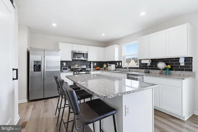 a kitchen with stainless steel appliances granite countertop a stove a sink a microwave a refrigerator and white cabinets