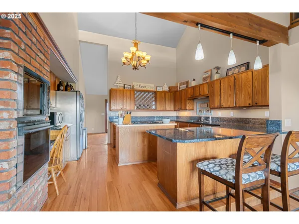 a open kitchen with stainless steel appliances granite countertop a refrigerator a sink dishwasher a stove and a dining table with wooden floor