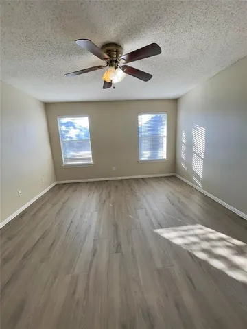 an empty room with wooden floor chandelier fan and windows
