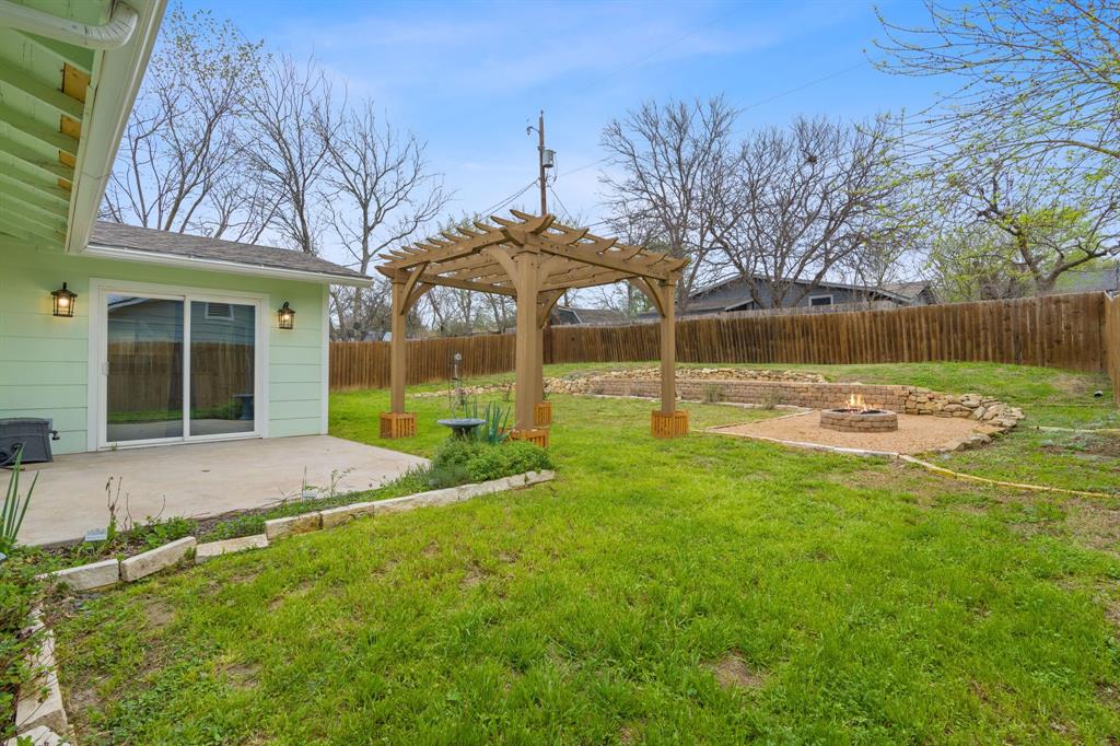 5211 Halmark Drive Austin, TX 78723 - Photo 22 of 27 An inviting backyard retreat features a wooden pergola, concrete patio, and a stone-lined fire pit, perfect for outdoor gatherings.
