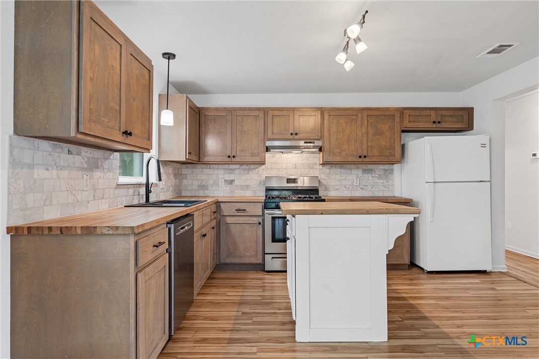 407 East 7th Street Cameron, TX 76520 - Photo 14 of 43 a kitchen with stainless steel appliances granite countertop a stove a sink dishwasher and a refrigerator with wooden floor