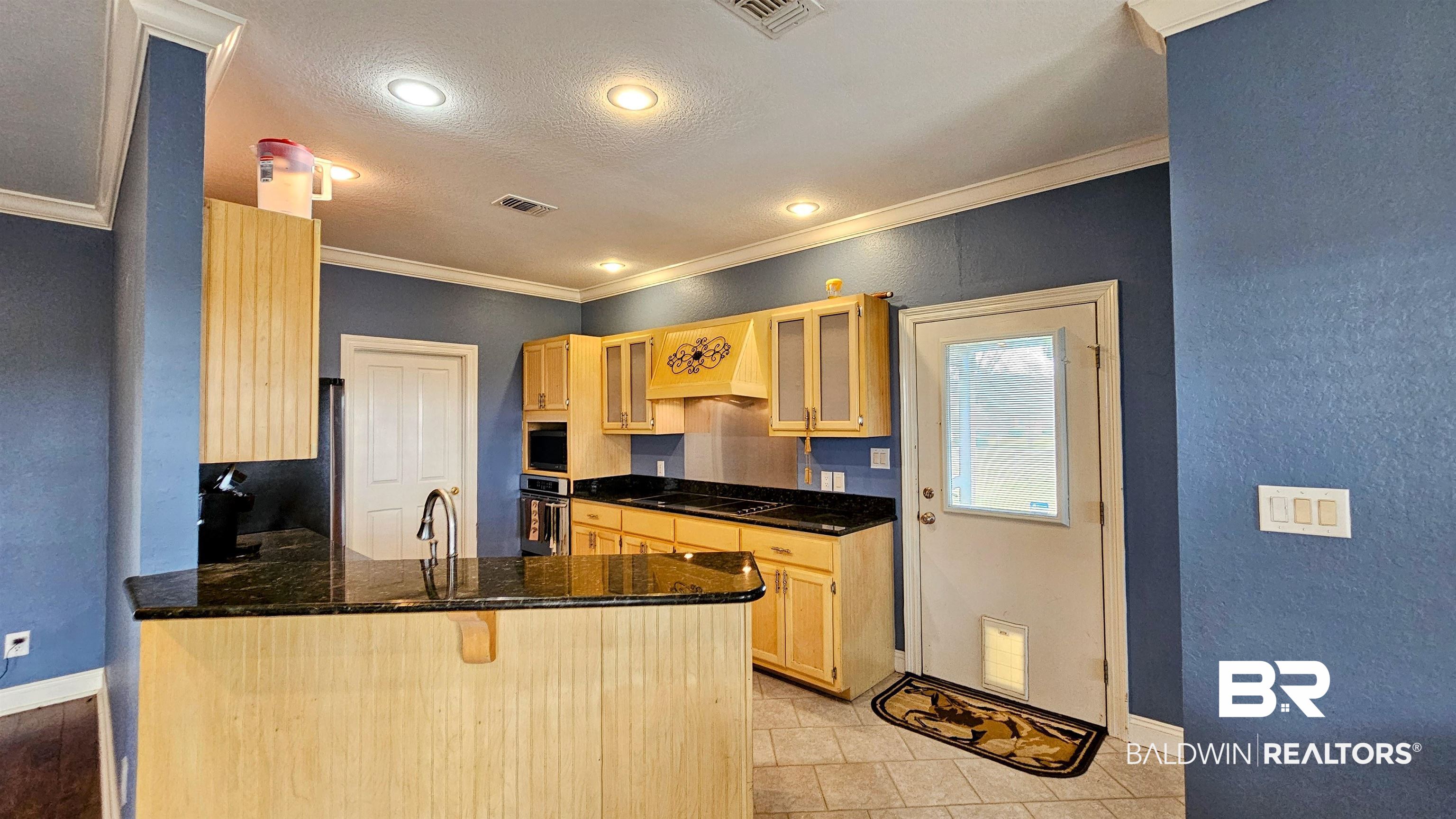9275 Crawford Road Elberta, AL 36530 - Photo 23 of 28 Kitchen with light brown cabinetry, a textured wall, a peninsula, glass insert cabinets, and premium range hood