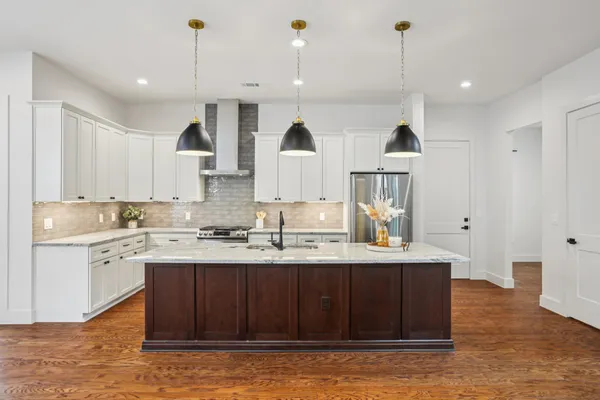 a kitchen with stainless steel appliances granite countertop a stove a sink a refrigerator and white cabinets with wooden floor