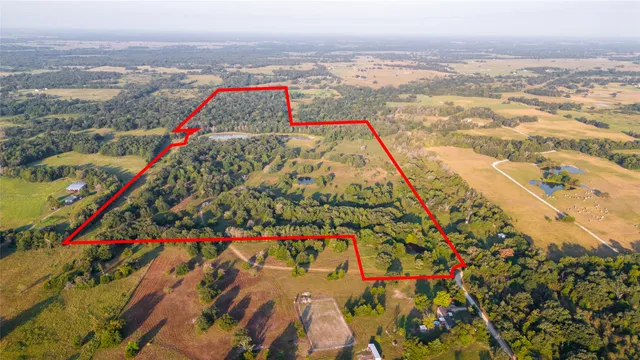 an aerial view of a residential houses with outdoor space and trees all around