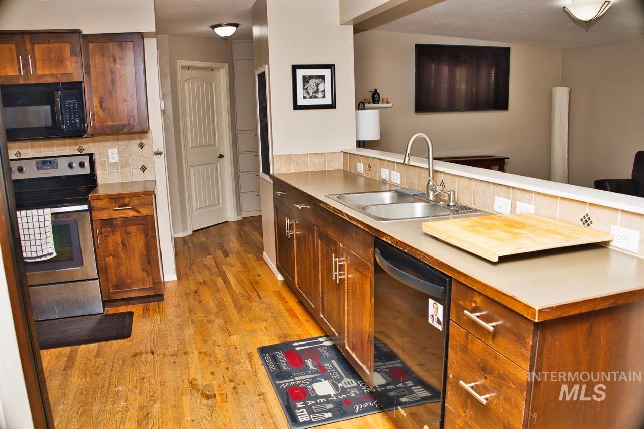 2223 West Spaulding Street Boise, ID 83705 - Photo 10 of 50 Kitchen featuring black appliances, light countertops, light wood finished floors, decorative backsplash, and wood finish cabinets
