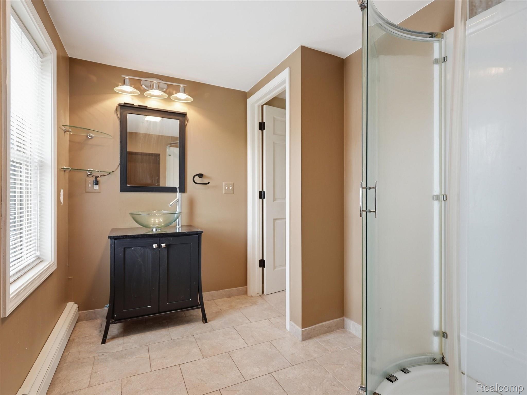 117 Kenyon Road Algonac, MI 48001 - Photo 34 of 47 Bathroom featuring a black vanity with a glass vessel sink, an integrated shower stall with a curved glass door, and neutral-toned tile flooring