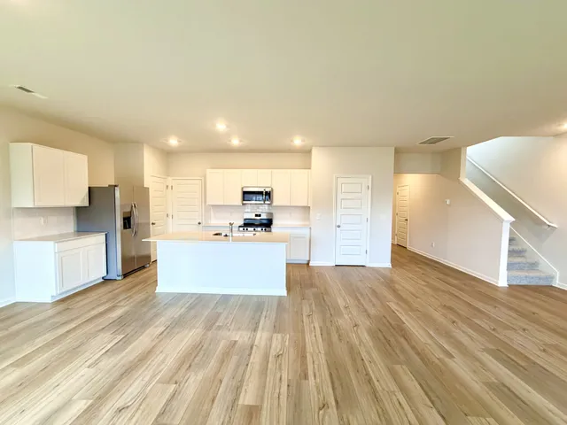 a large kitchen with kitchen island a stove a refrigerator white cabinets and wooden floor