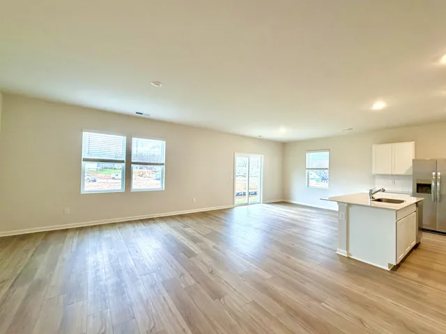 a view of a kitchen and an empty room with wooden floor and a window