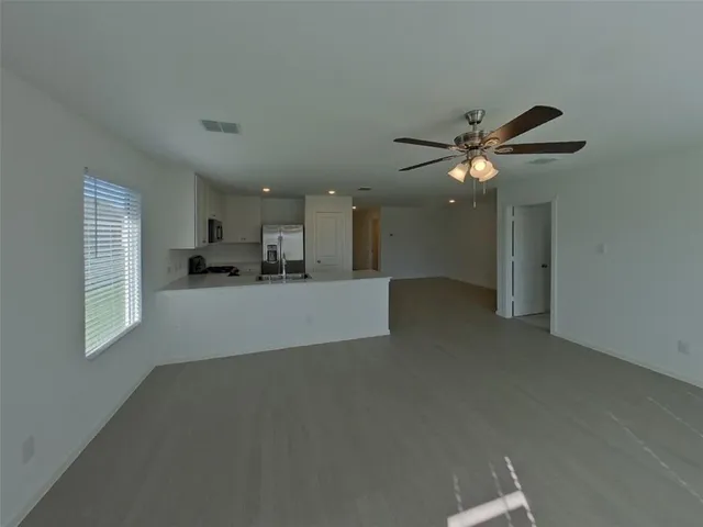 a view of an empty room with kitchen and window