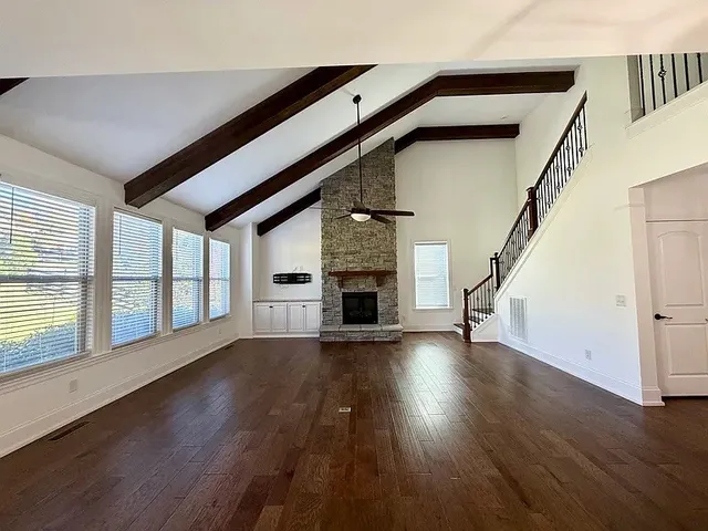a view of an empty room with wooden floor fireplace and windows