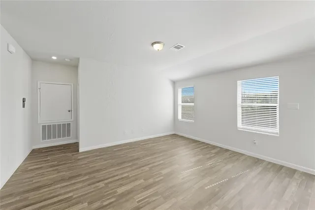 a view of an empty room with wooden floor and a window