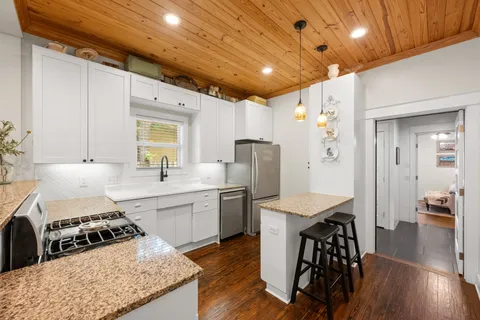 a kitchen with stainless steel appliances granite countertop a stove a refrigerator a sink dishwasher a dining table and chairs with wooden floor