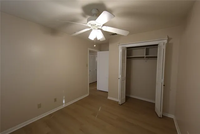 an empty room with wooden floor closet and fan