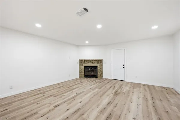 a view of an empty room with wooden floor and a fireplace