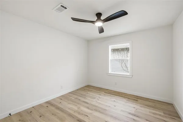 an empty room with wooden floor ceiling fan and windows