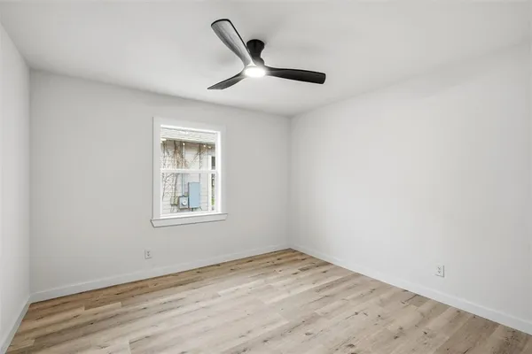 an empty room with wooden floor ceiling fan and window