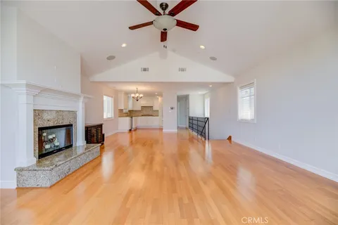 a big room with wooden floor a fireplace a ceiling fan and windows