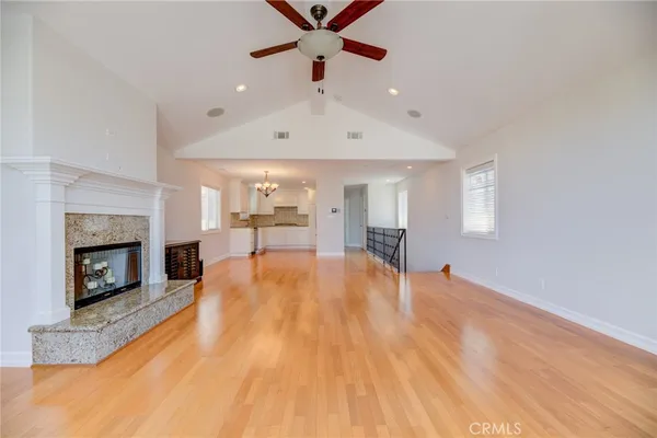 a big room with wooden floor a fireplace a ceiling fan and windows