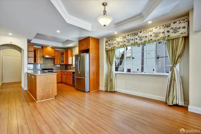 a kitchen with stainless steel appliances granite countertop a refrigerator a sink dishwasher a stove and a dining table with wooden floor