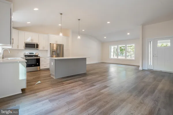 a kitchen with kitchen island a refrigerator a sink dishwasher a stove and white cabinets with wooden floor