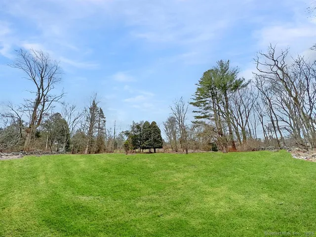a view of a building in front of a big yard with plants and large trees