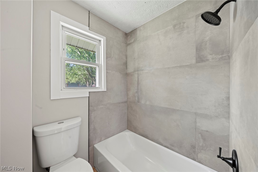 1218 Briggle Road Akron, OH 44320 - Photo 21 of 40 Bathroom featuring a white bathtub, gray large format wall tiles, a white window with exterior greenery, and a dark finish shower head