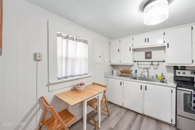 a kitchen with stainless steel appliances granite countertop a stove a sink dishwasher and white cabinets with wooden floor