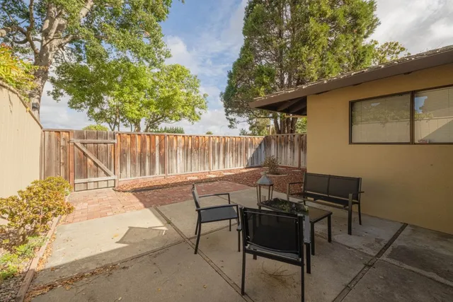a view of a patio with table and chairs with wooden fence and large trees