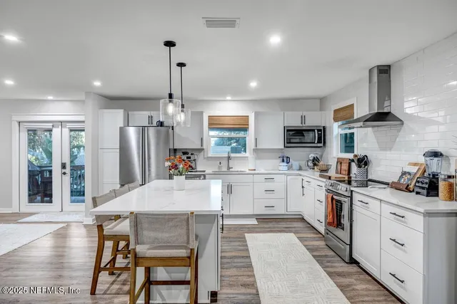 a kitchen with stainless steel appliances granite countertop a refrigerator a stove and white cabinets with wooden floors