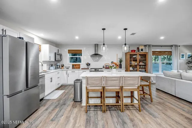 a large white kitchen with a stove a sink dishwasher and a refrigerator with wooden floor