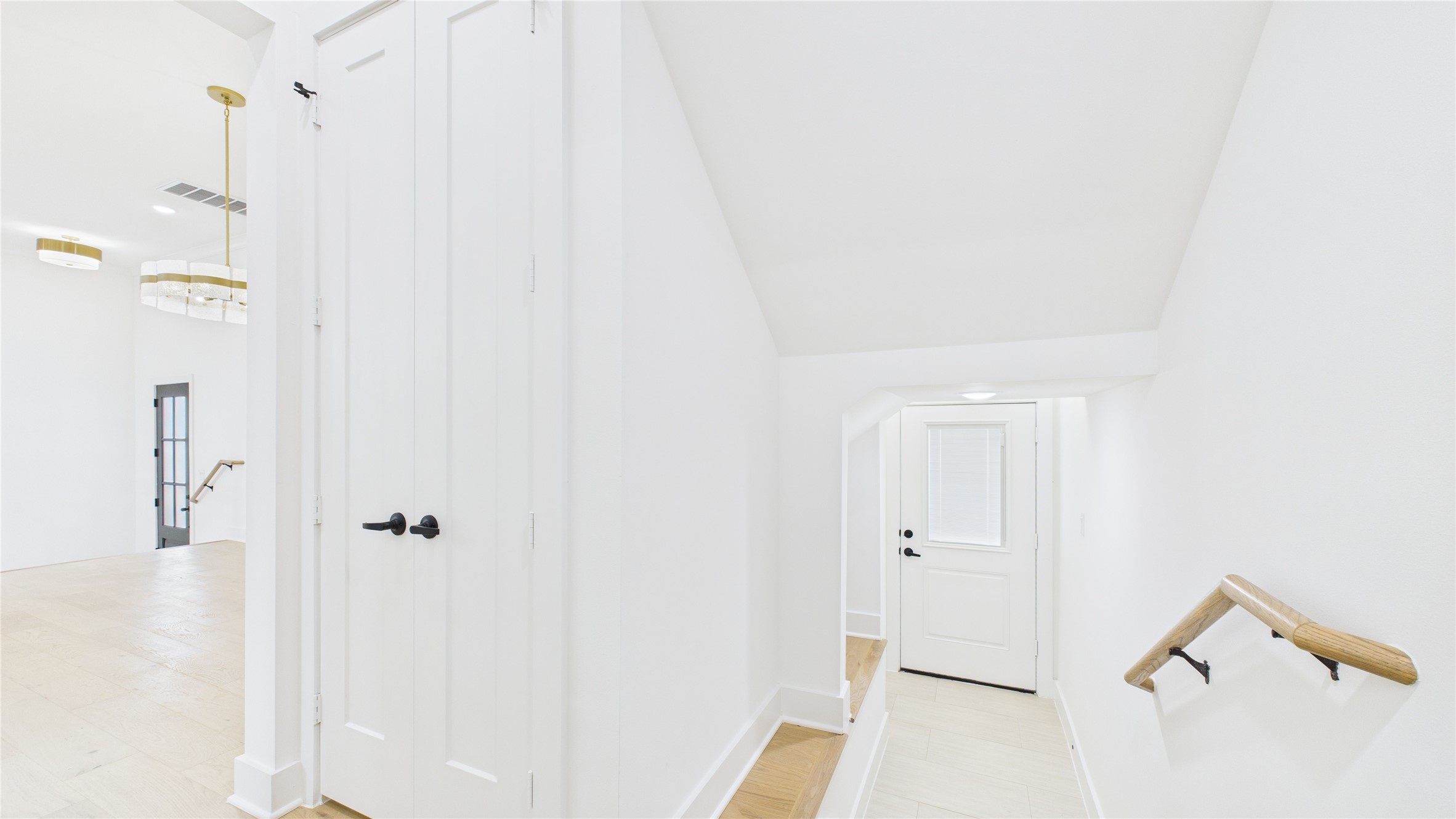 602 Jewett Street, Unit A Houston, TX 77009 - Photo 12 of 44 Bright and modern hallway with white walls and light wood floors. Features a staircase with a wooden handrail, a double door closet, and stylish light fixtures.