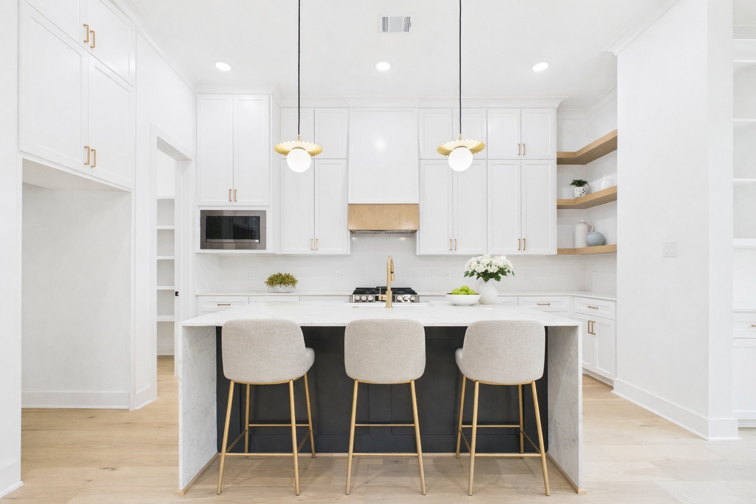 602 Jewett Street, Unit A Houston, TX 77009 - Photo 2 of 46 Bright and spacious kitchen with modern design, featuring sleek white cabinetry, a large central island with a dark accent, and elegant pendant lighting. The space includes stainless steel appliances, ample natural light from large windows, and light wood flooring, creating a welcoming and functional environment.