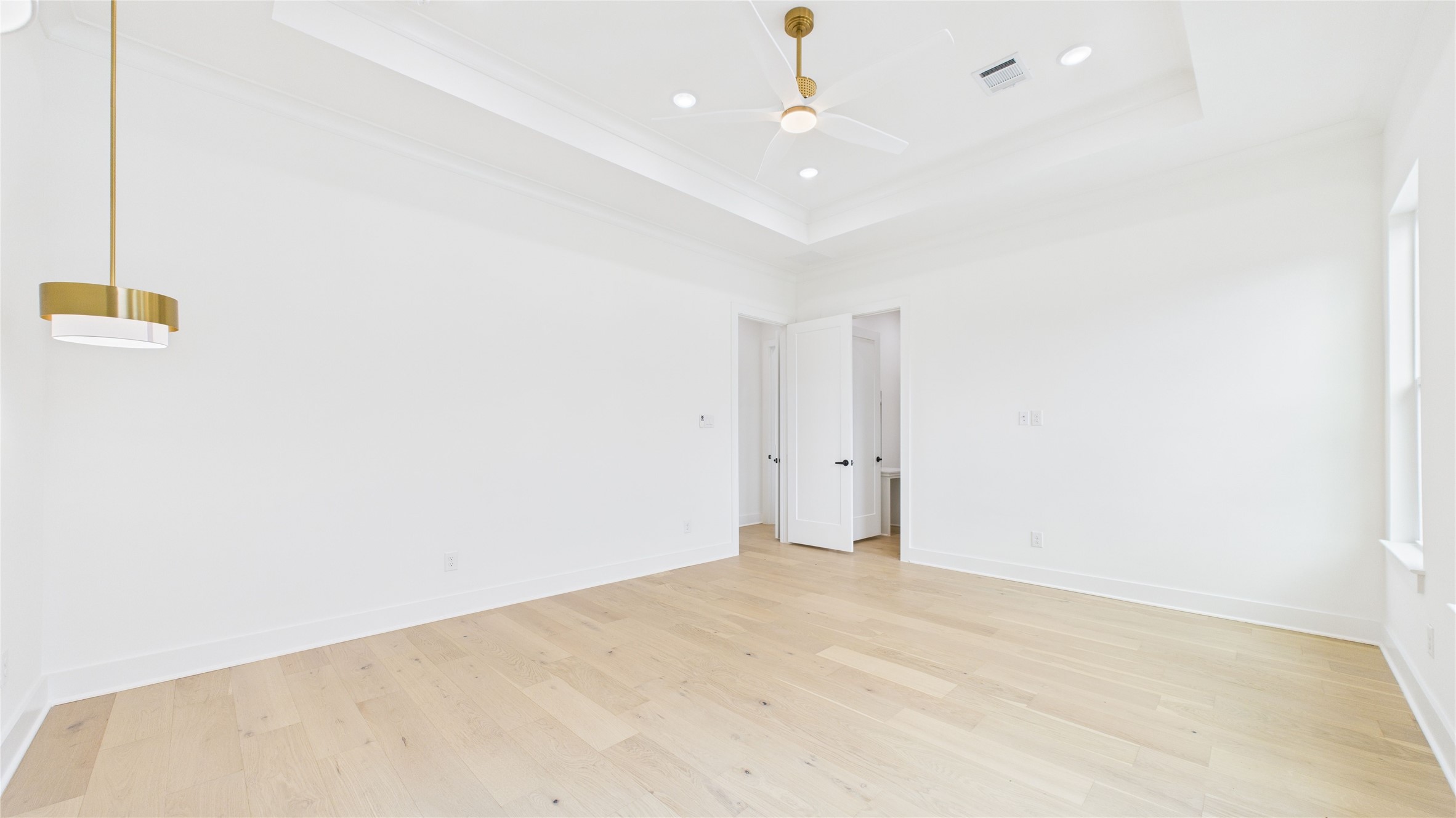 602 Jewett Street, Unit A Houston, TX 77009 - Photo 25 of 46 Bright, spacious primary bedroom with light hardwood floors and white walls. Features a modern ceiling fan, recessed lighting, and a stylish pendant light. The room has a tray ceiling and a doorway leading to an adjacent area.