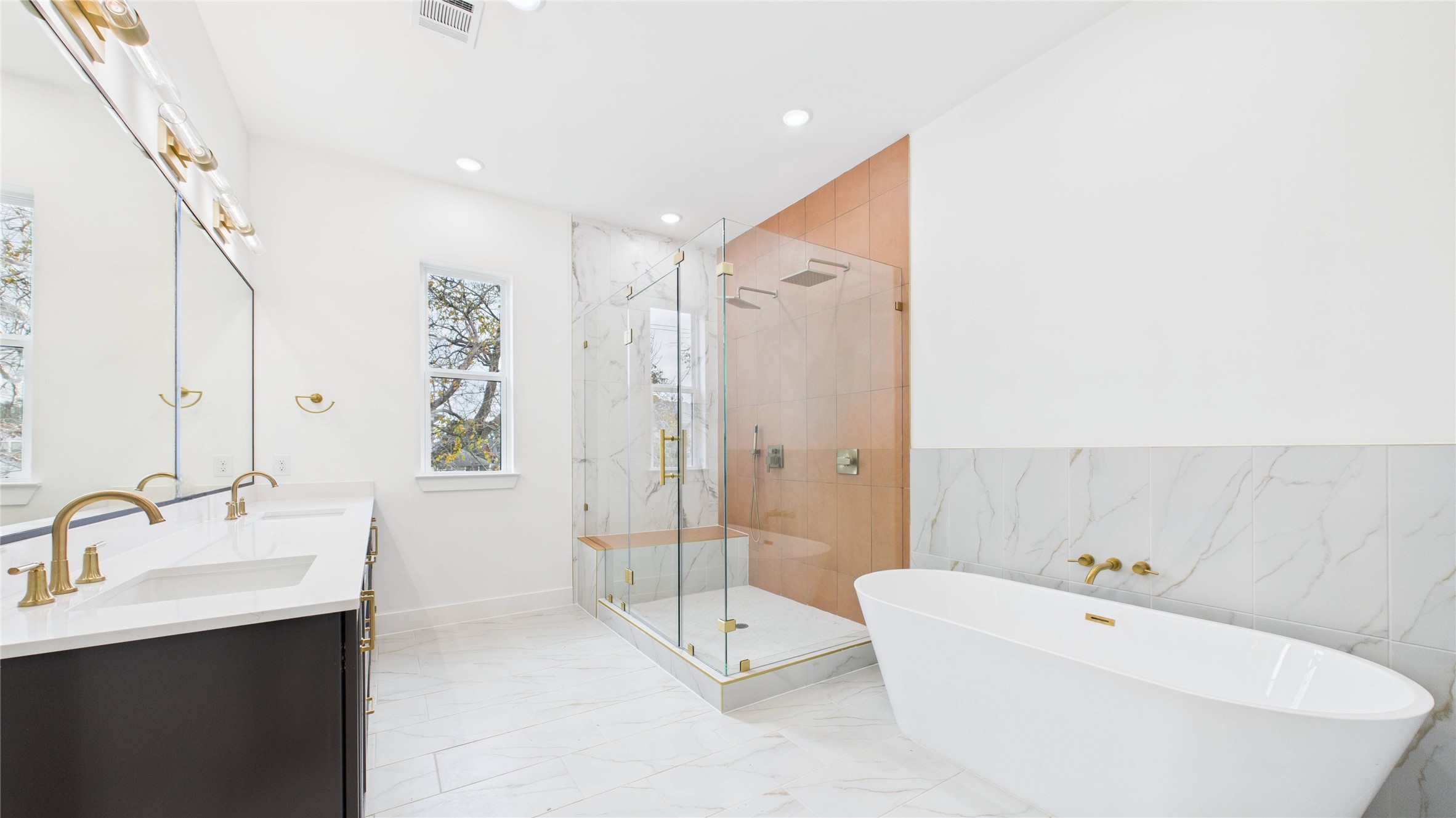 602 Jewett Street, Unit A Houston, TX 77009 - Photo 26 of 44 The primary bathroom features a spacious walk-in glass shower with two rainheads and a spray wand, a freestanding bathtub with gold fixtures, and a double vanity with elegant lighting. The room is bright and sleek.