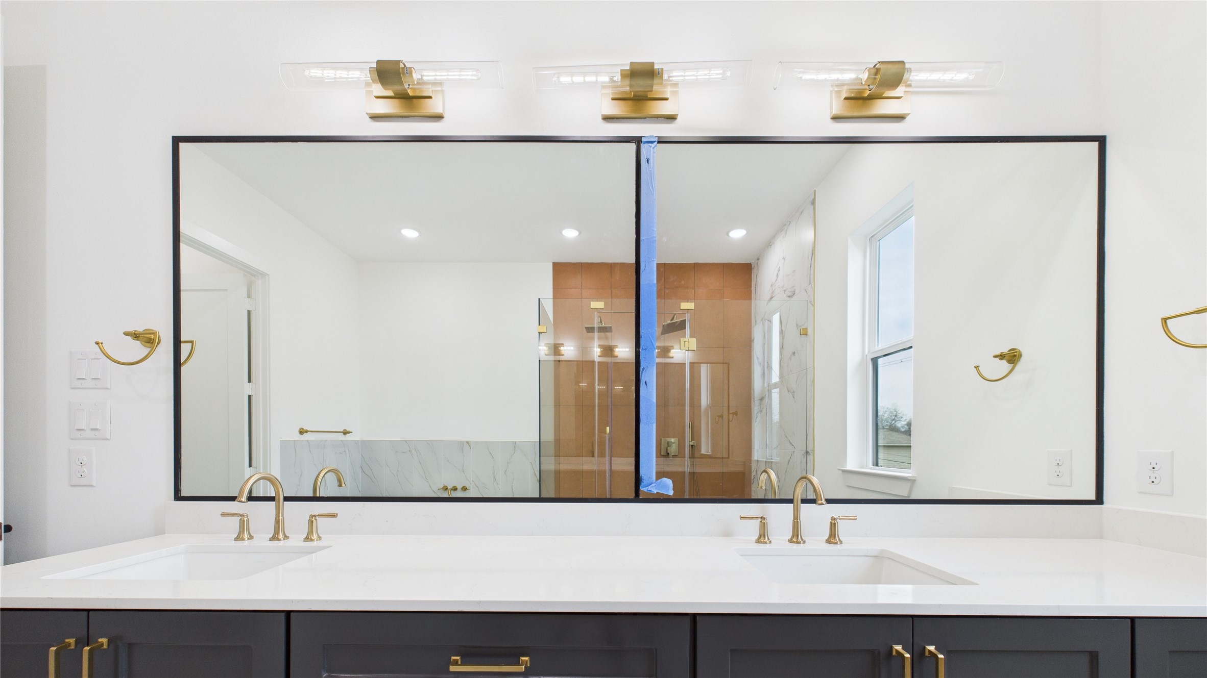 602 Jewett Street, Unit A Houston, TX 77009 - Photo 30 of 46 This modern bathroom features a double vanity with sleek quartz countertops and gold fixtures. The large mirror is framed and illuminated by stylish light fixtures. The room has a bright, clean look, enhanced by natural light from a nearby window.