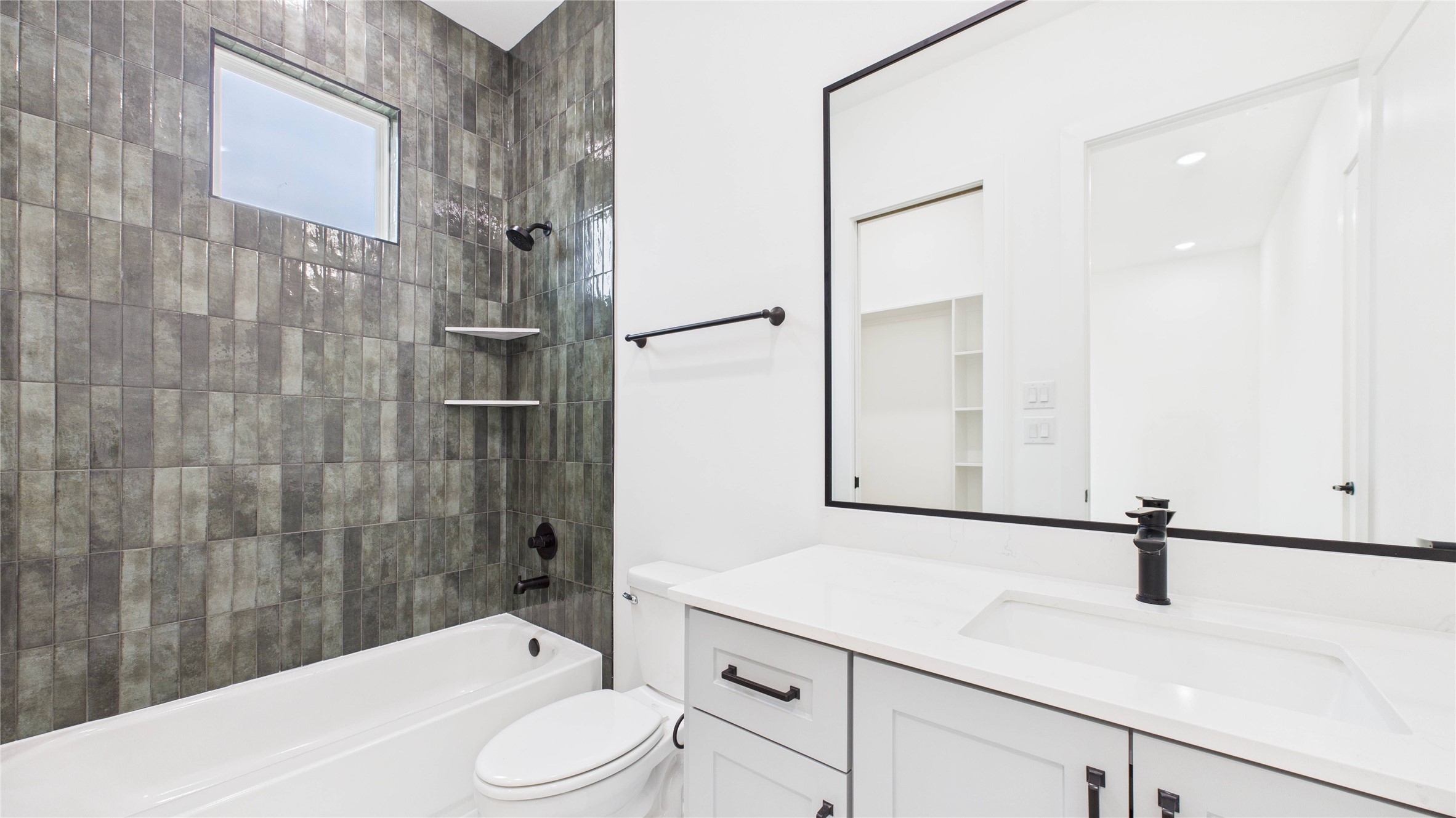 602 Jewett Street, Unit A Houston, TX 77009 - Photo 38 of 44 This modern bathroom features sleek, dark tiled walls that reach to the ceiling, with a built-in bathtub and shower. It has a large mirror above a white vanity with black fixtures, providing a clean and stylish look.