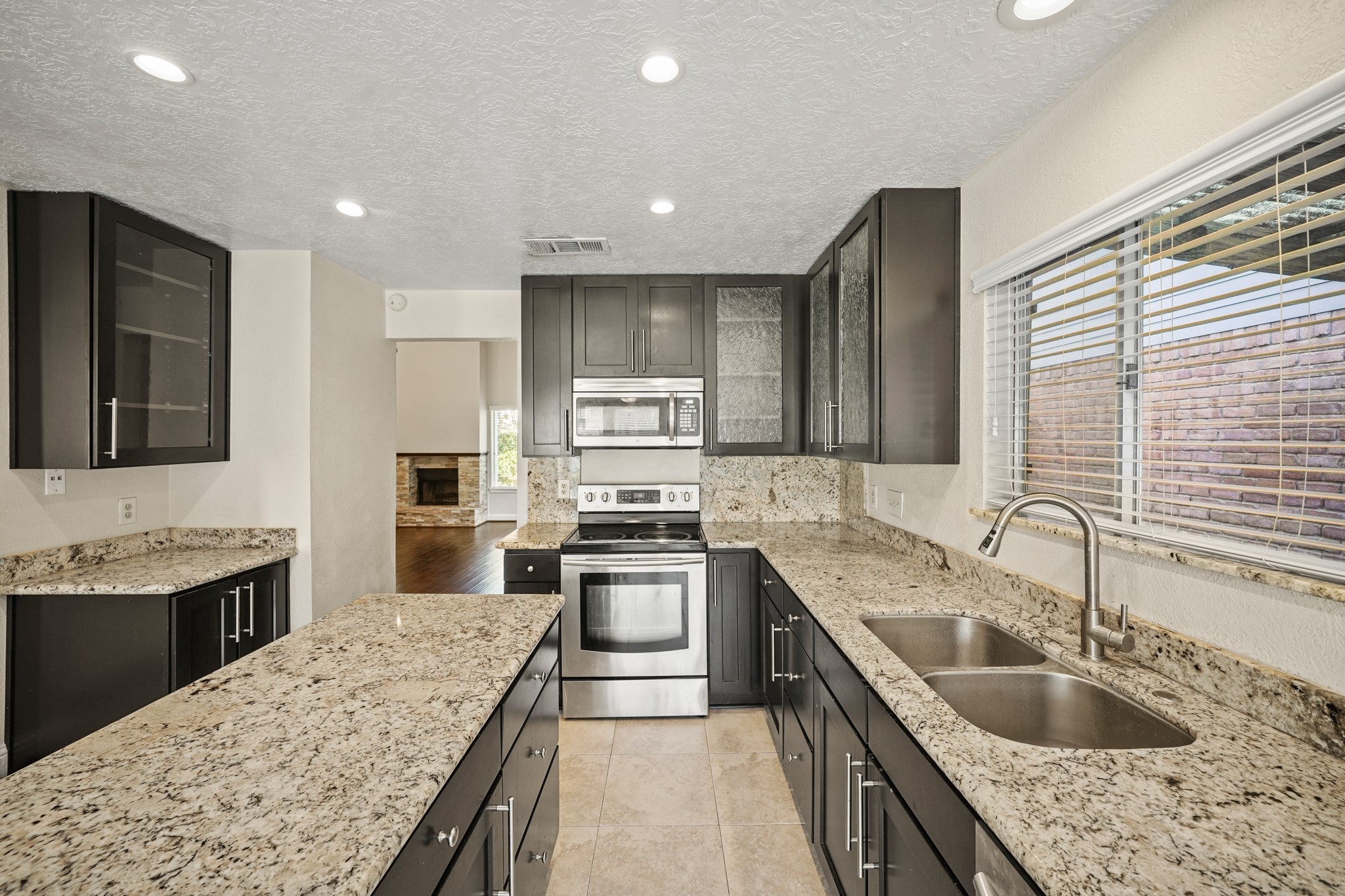 1641 Beaconshire Houston, TX 77077 - Photo 12 of 27 In the kitchen, rich dark cabinetry pairs beautifully with the light granite countertops and matching backsplash, offering a clean, modern contrast. Stainless steel appliances—including a built-in microwave, electric range, and dishwasher—enhance both style and convenience.