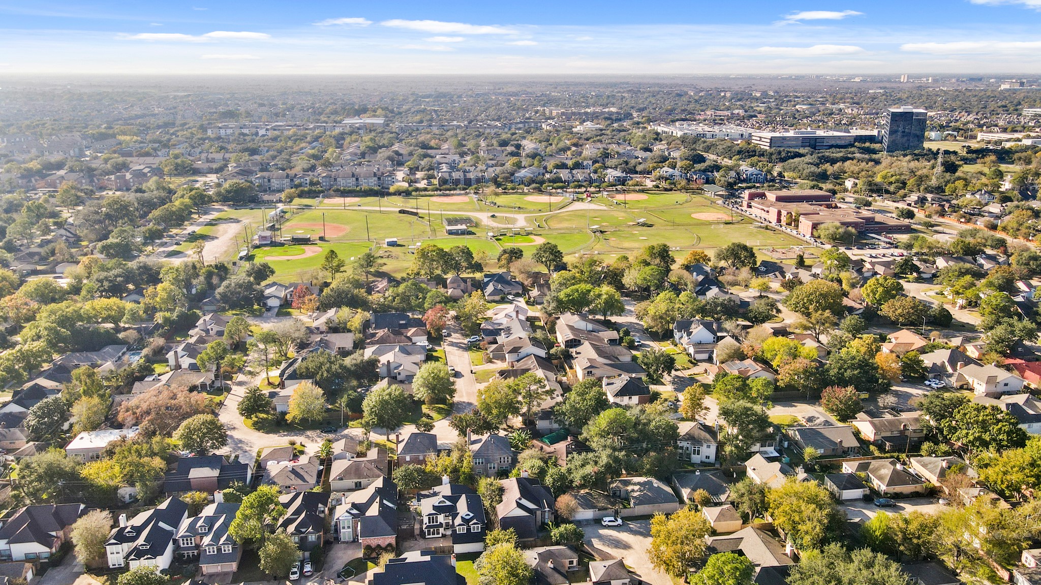 1641 Beaconshire Houston, TX 77077 - Photo 5 of 27 This aerial photo captures a picturesque view of a peaceful, tree-lined neighborhood surrounded by lush greenery and community amenities. At the center of the image is a large recreational complex featuring multiple baseball and softball fields, open green space, and walking areas—perfect for outdoor activities and community gatherings.