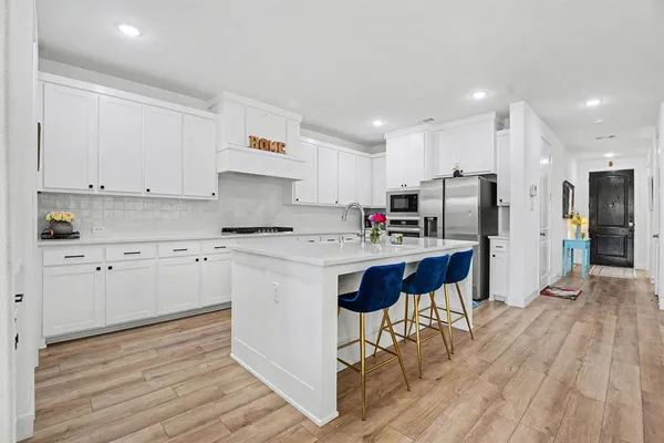 a kitchen with stainless steel appliances a stove top oven a refrigerator and white cabinets with wooden floor